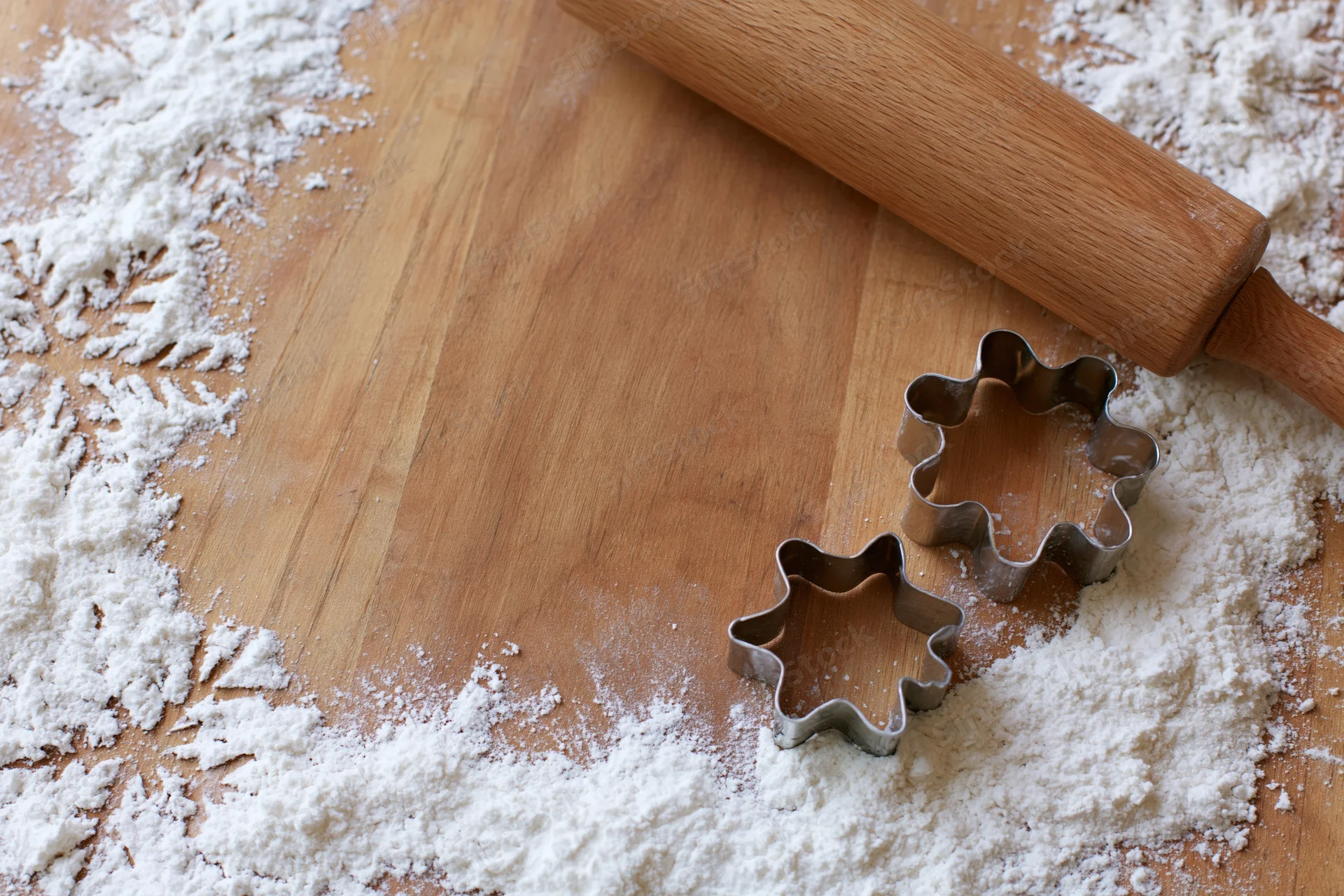 Star and snowflake cookie cutters on a floured wooden board with a rolling pin nearby