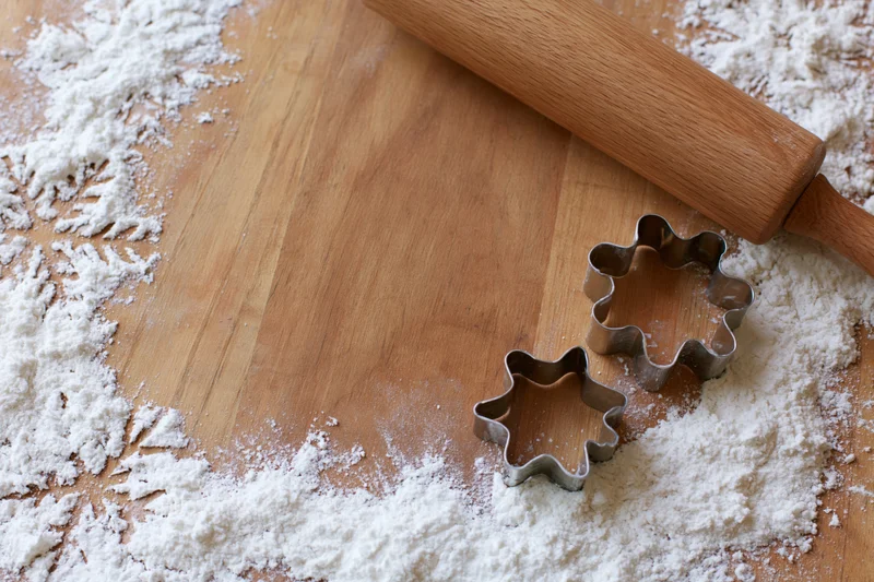 Star and snowflake cookie cutters on a floured wooden board with a rolling pin nearby