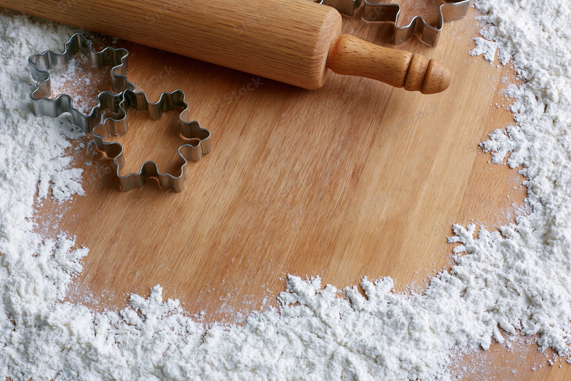Wooden rolling pin and star-shaped cookie cutters on a floured cutting board
