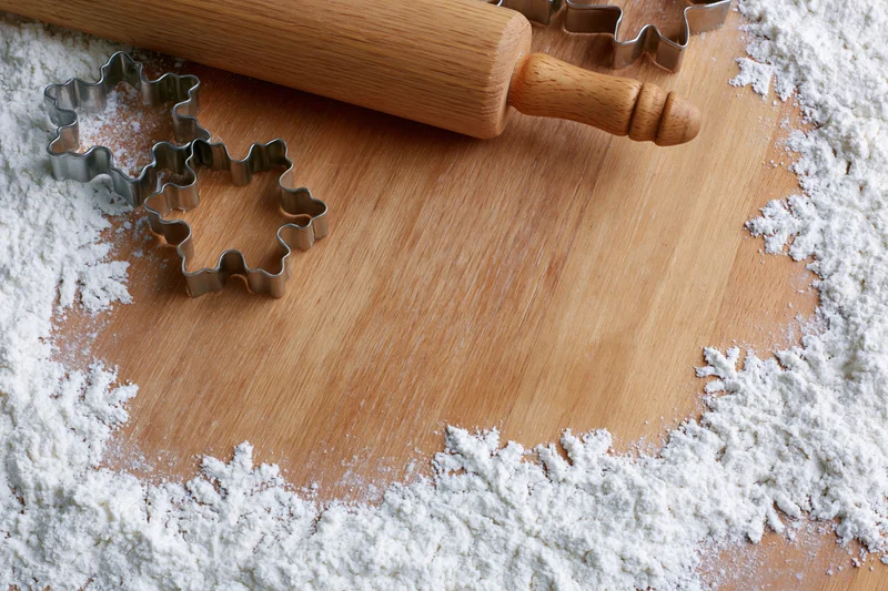 Wooden rolling pin and star-shaped cookie cutters on a floured cutting board