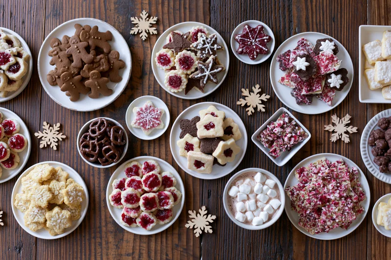Assorted holiday cookies and sweets arranged on a wooden table with snowflake decorations