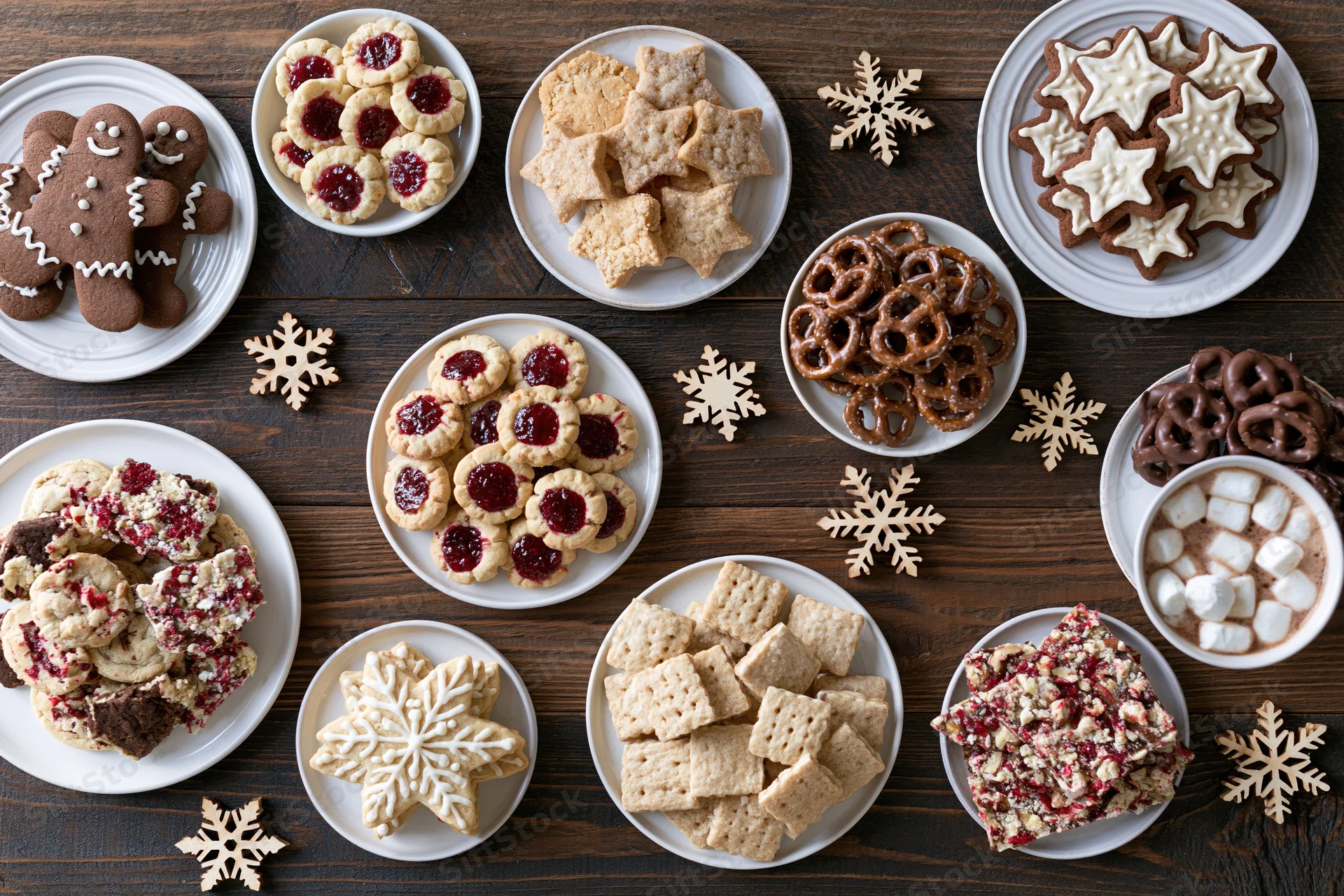 Assorted christmas cookies and sweets arranged on white plates on a dark wooden table with snowflake decorations