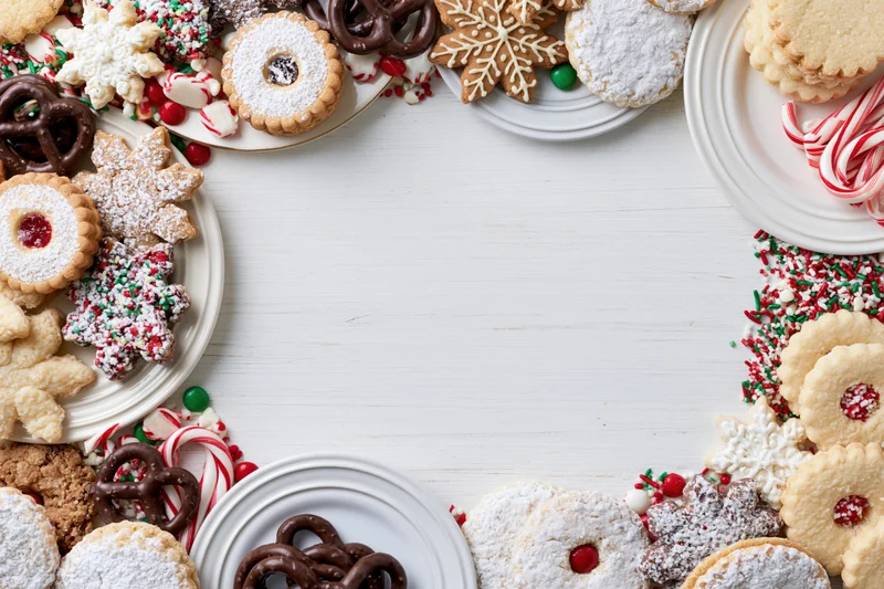 Assorted christmas cookies and candy arranged on white plates around a central copyspace on a white wooden table