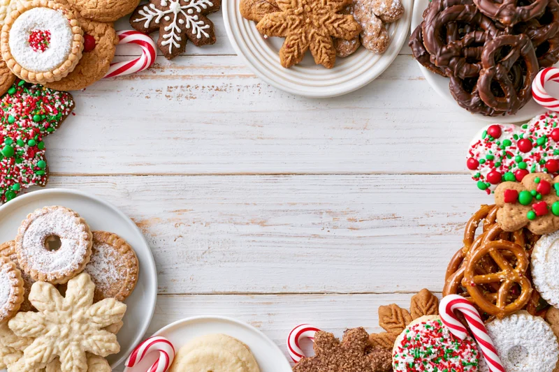 Assorted christmas cookies and candy arranged around white wooden table with copyspace in center