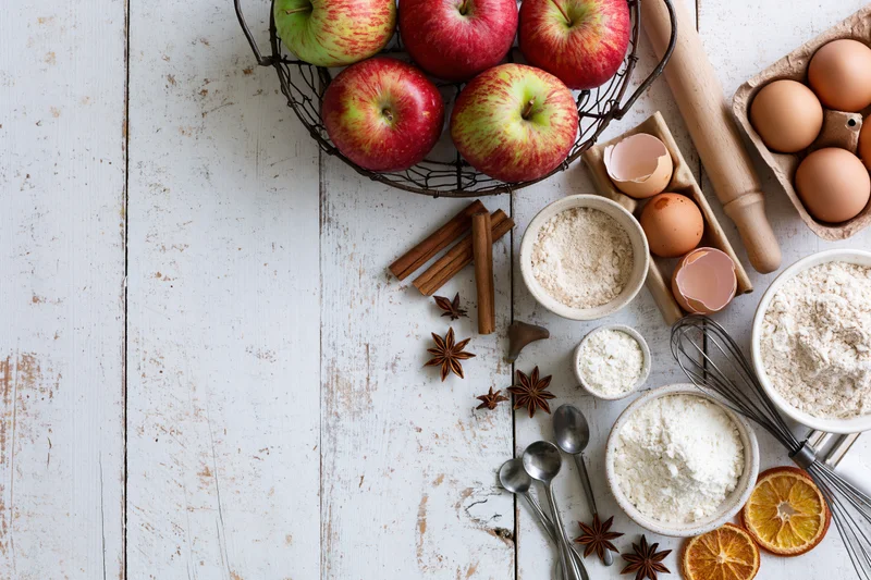 Apples and baking ingredients arranged on a white wooden table with copyspace on the left