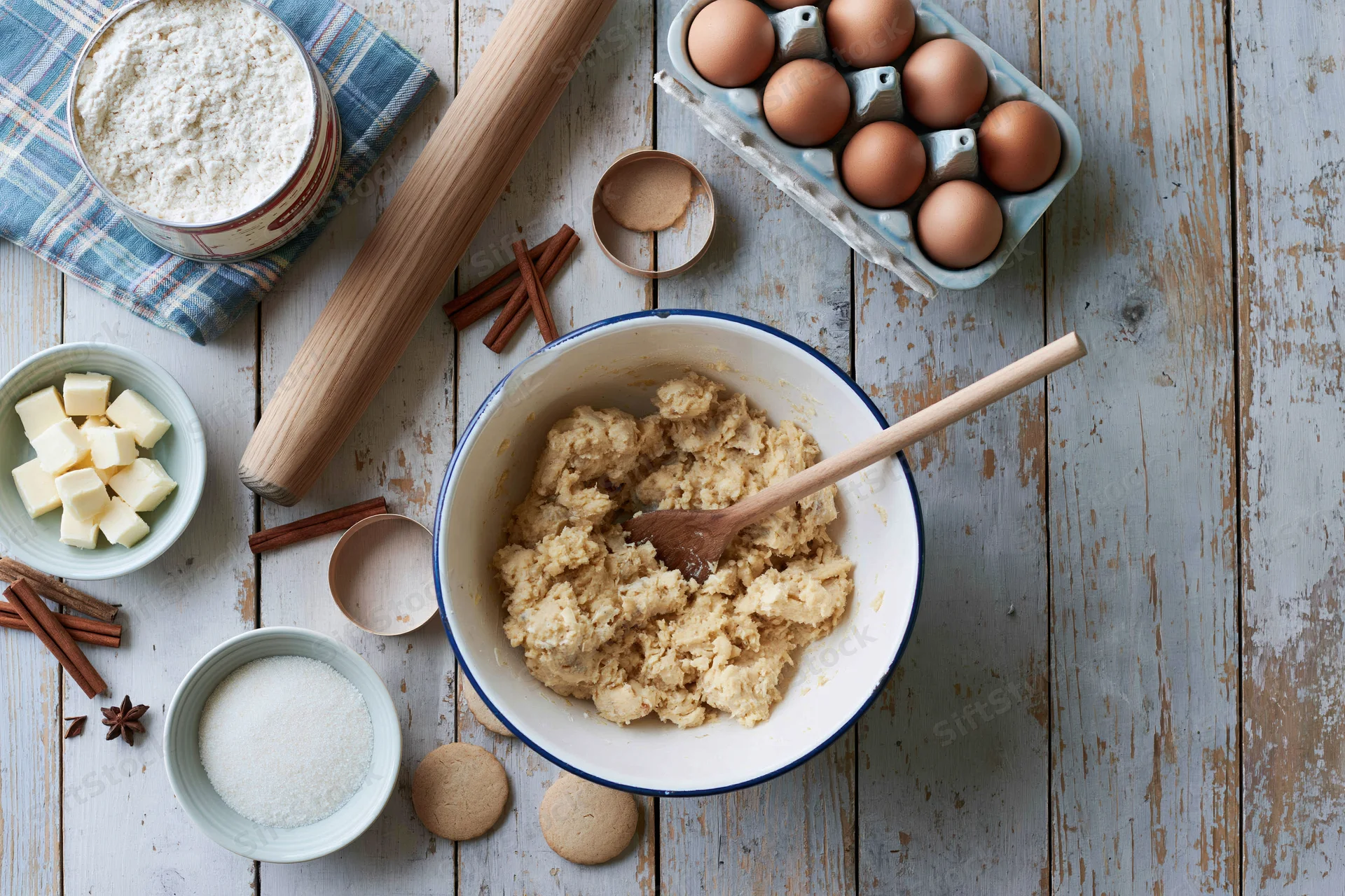 Dough mixture in a bowl with wooden spoon surrounded by baking ingredients on a rustic wooden table