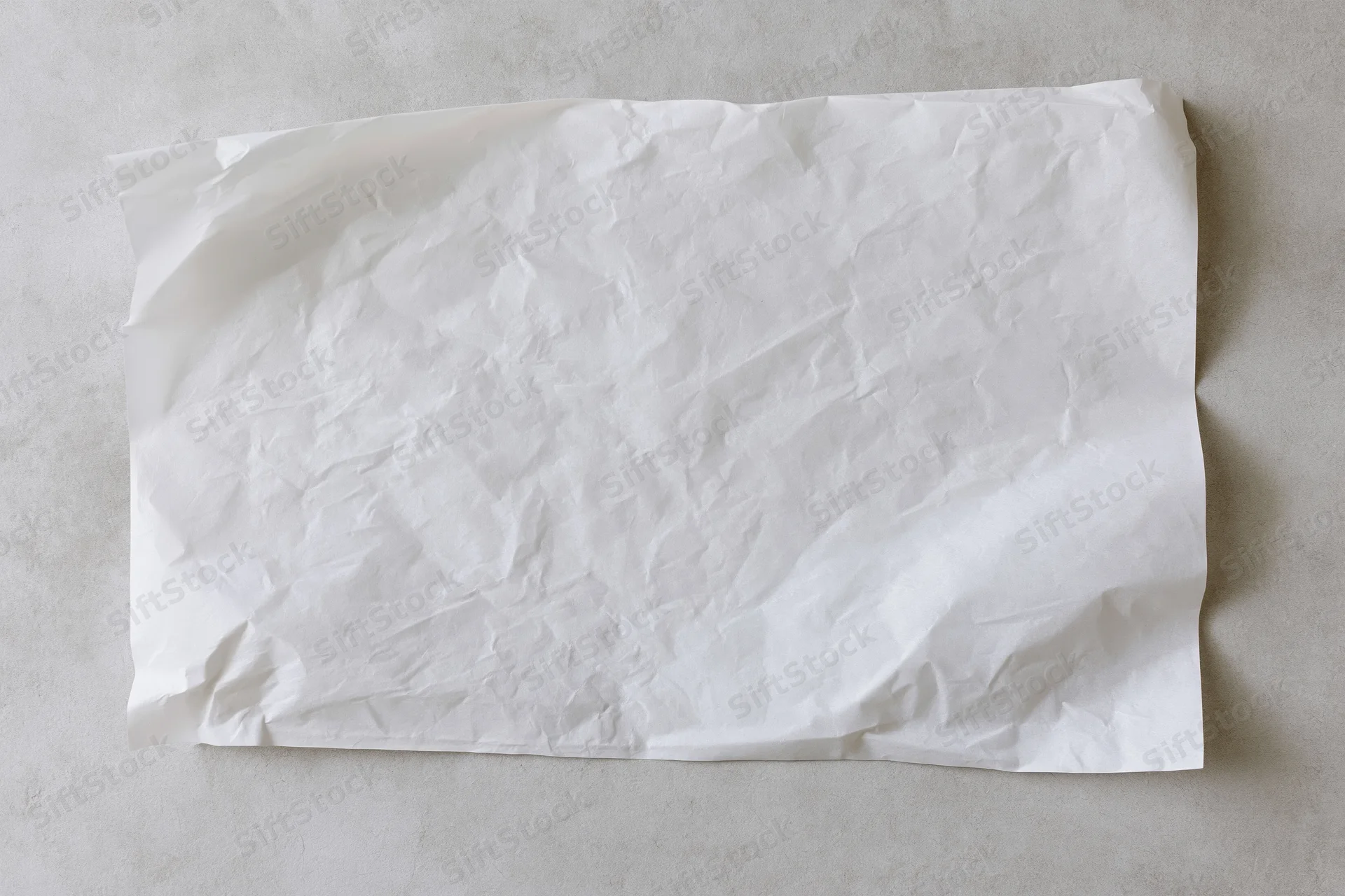 Crumpled white paper sheet lying flat on a gray concrete surface