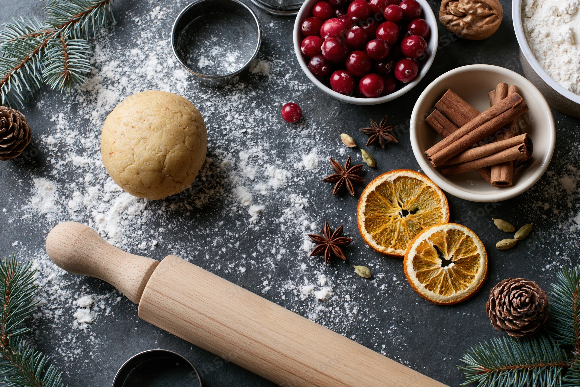 Dough ball and baking tools with spices and cranberries on dark countertop for holiday baking