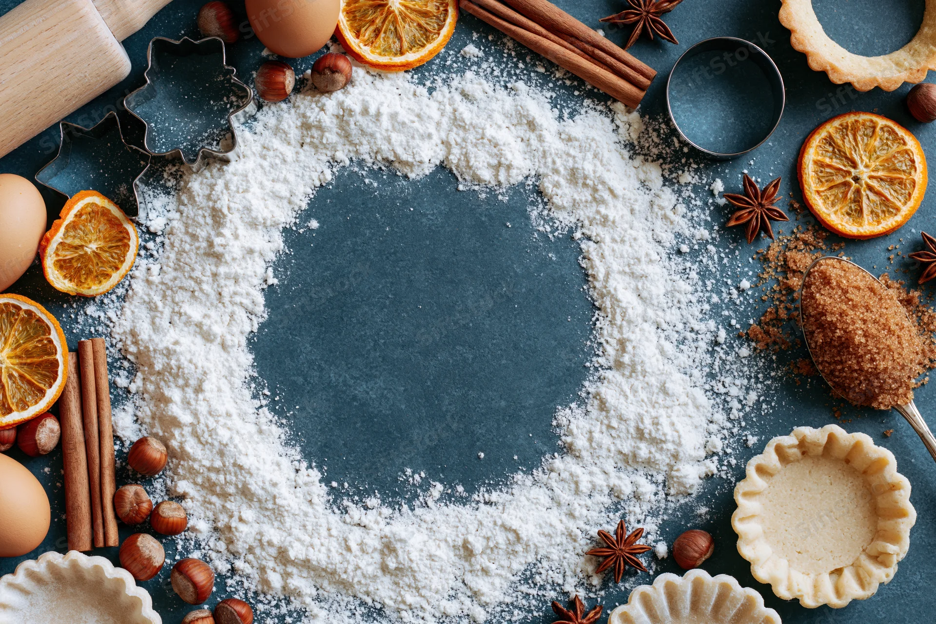 Flour arranged in a circle on a dark surface surrounded by baking ingredients and tools