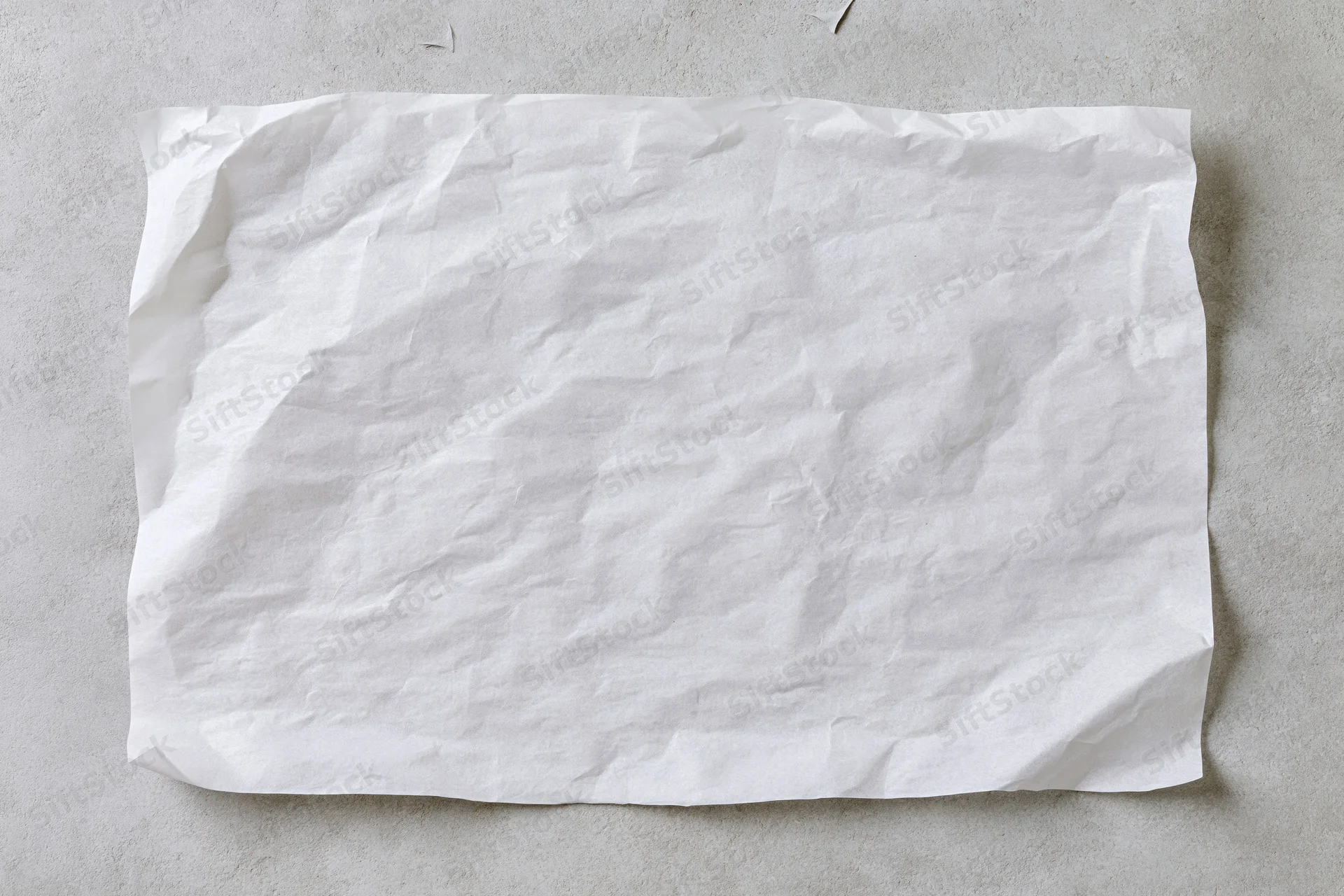 Crumpled white paper sheet lying flat on a gray concrete surface
