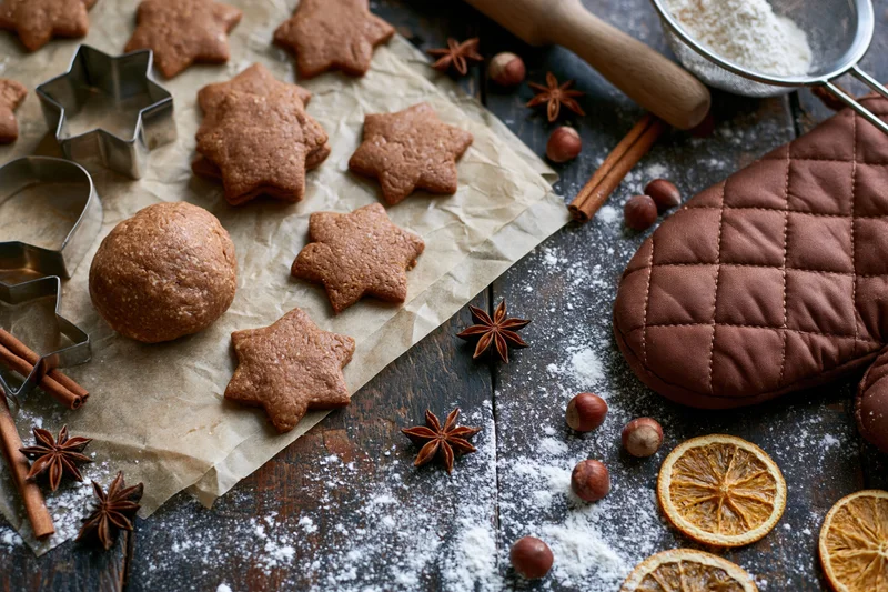 Star-shaped gingerbread cookies on parchment paper with spices and baking tools on a dark wooden table