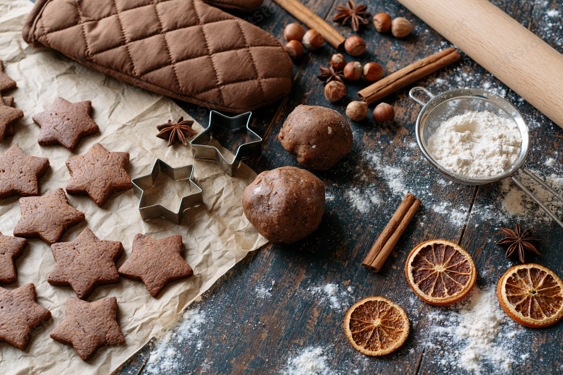 Star-shaped gingerbread cookies on parchment paper with dough, spices and baking tools on a dark wooden table