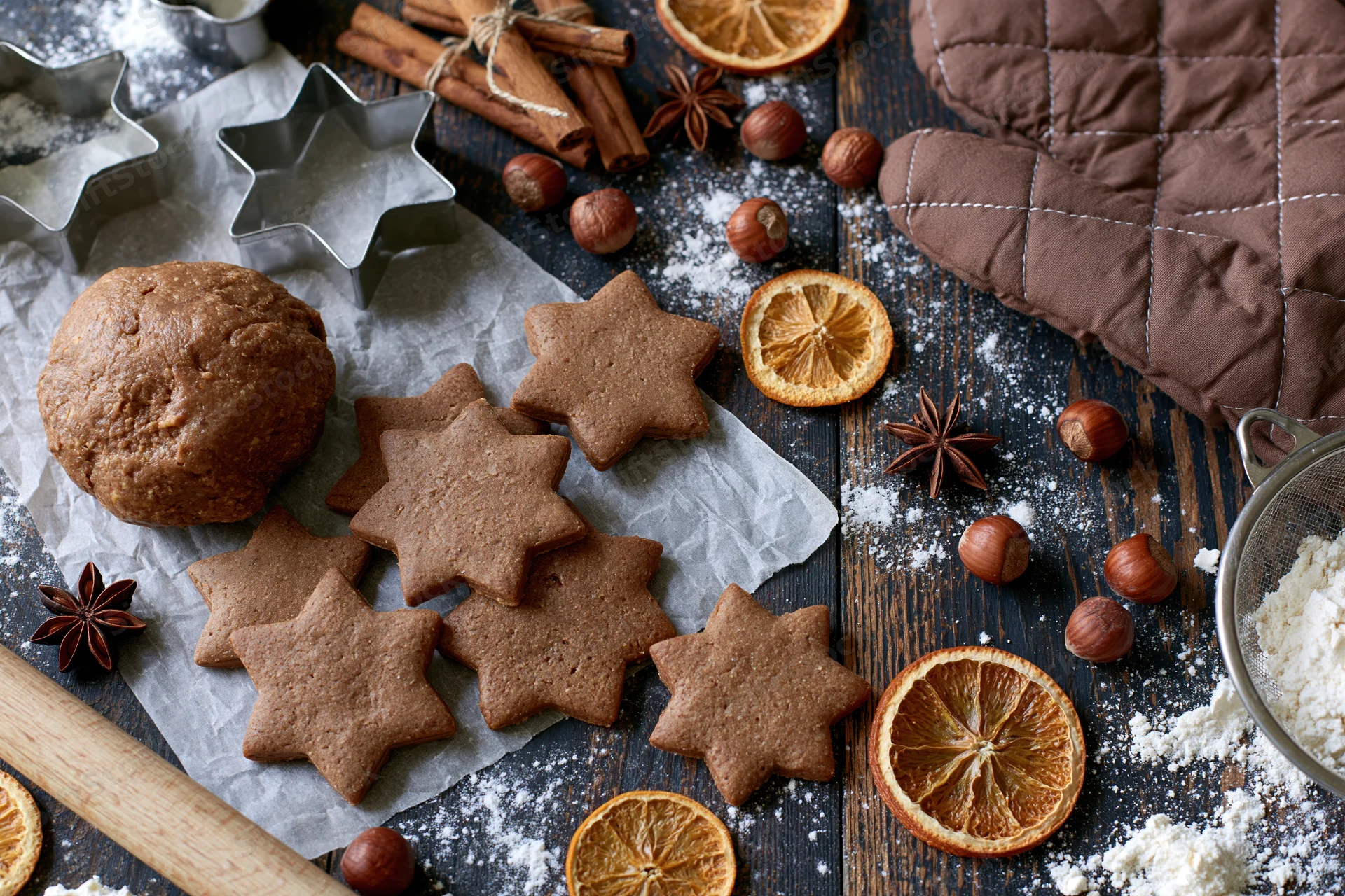 Star-shaped gingerbread cookies and dough on a wooden table with spices, dried oranges, and baking tools for holiday baking