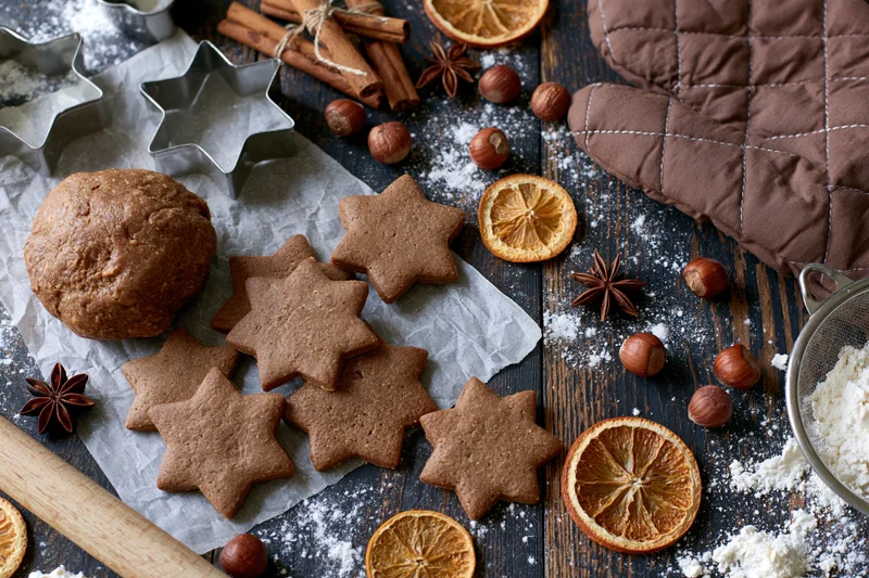 Star-shaped gingerbread cookies and dough on a wooden table with spices, dried oranges, and baking tools for holiday baking