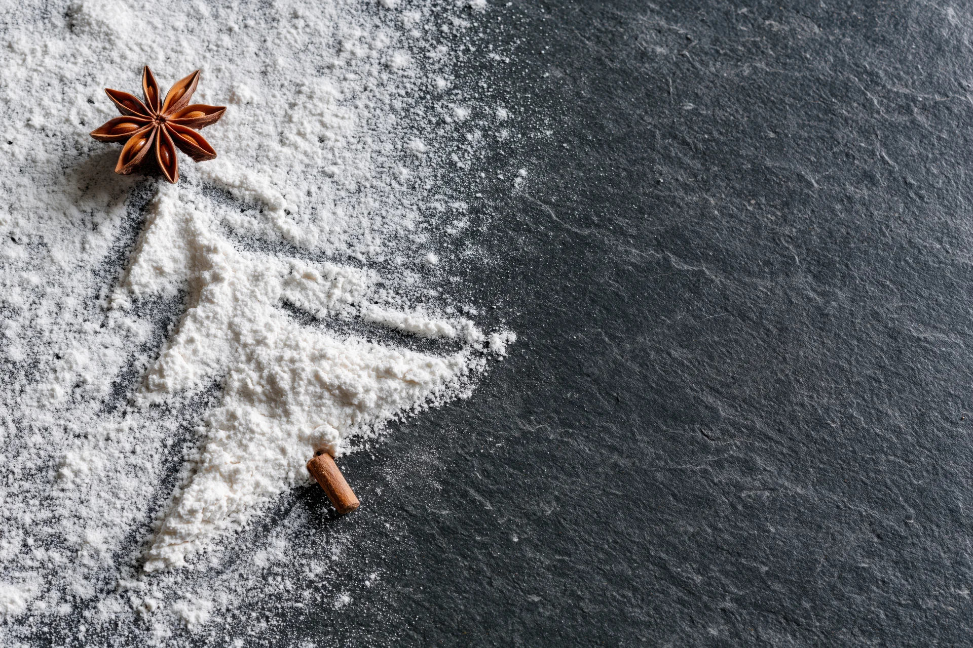 Flour and spices arranged on a dark slate surface with copyspace