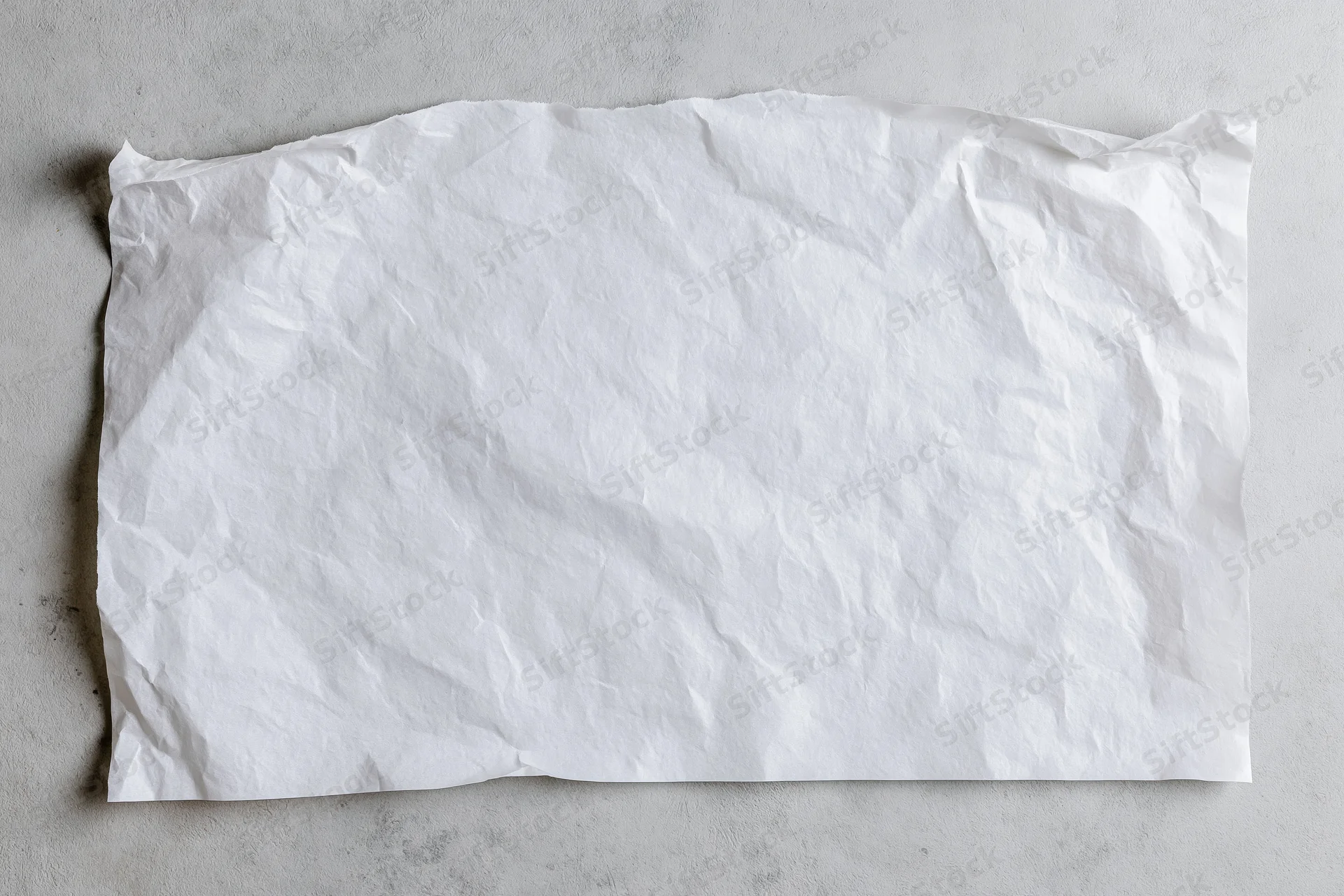 Crumpled white paper sheet lying flat on a gray concrete surface