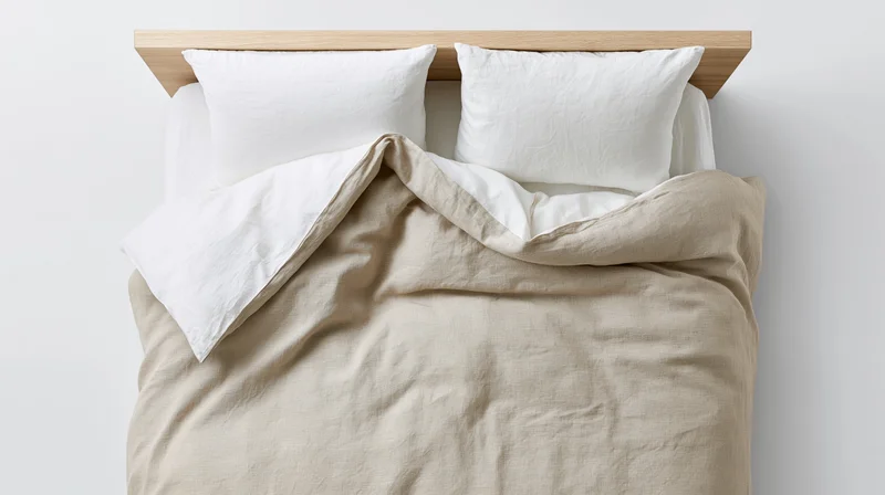 Unmade bed with white pillows and beige duvet against wooden headboard in minimalist bedroom