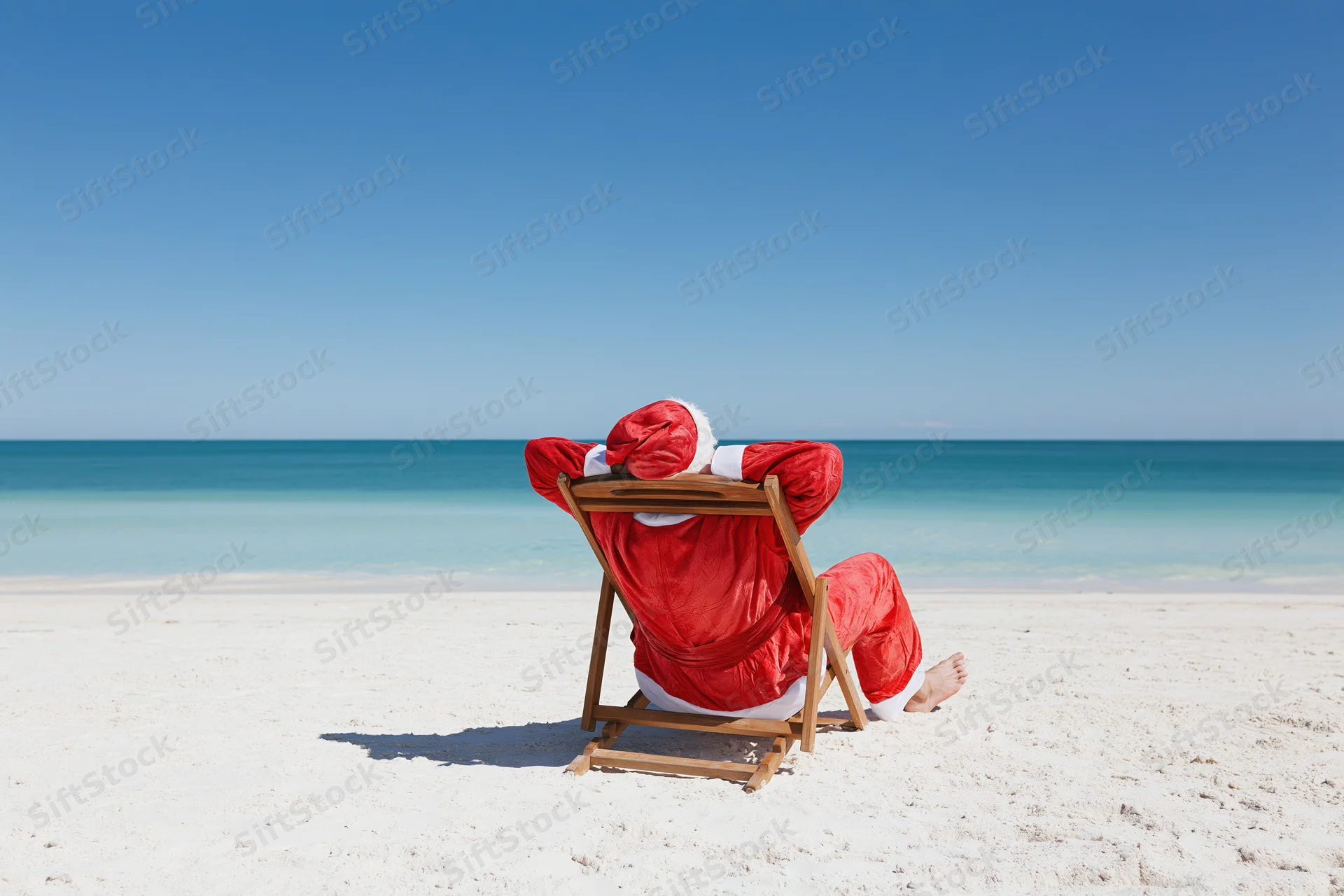 Santa reclining in a deckchair on a sandy beach facing the ocean