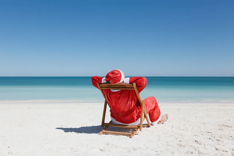 Santa reclining in a deckchair on a sandy beach facing the ocean
