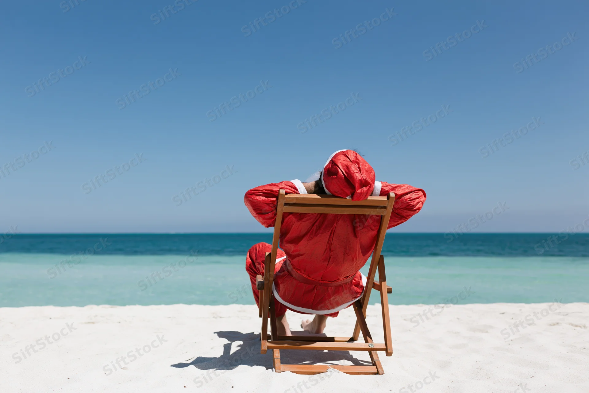 Santa reclining in a deckchair on a sandy beach facing the ocean