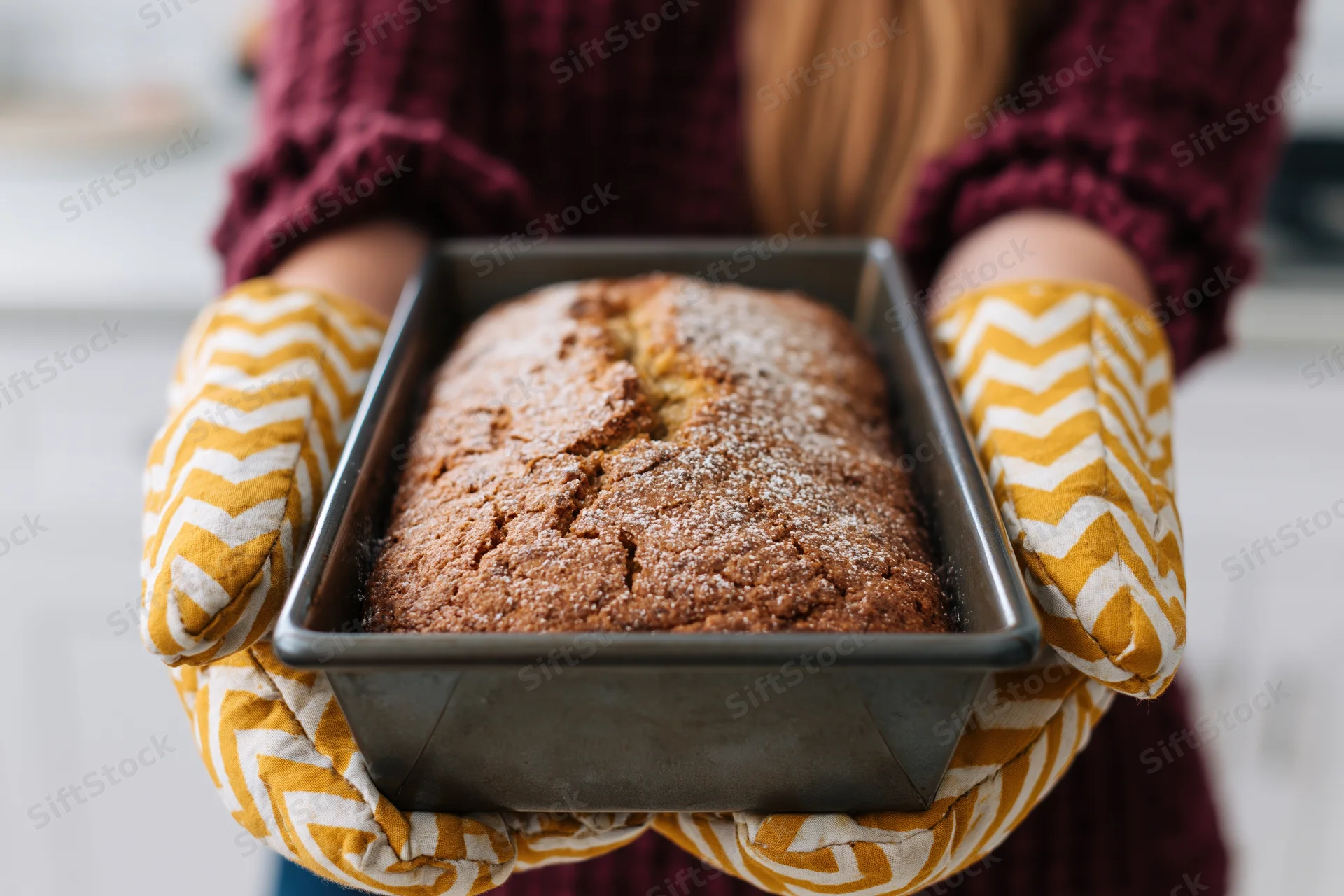 Woman holding freshly baked loaf in oven mitts in kitchen