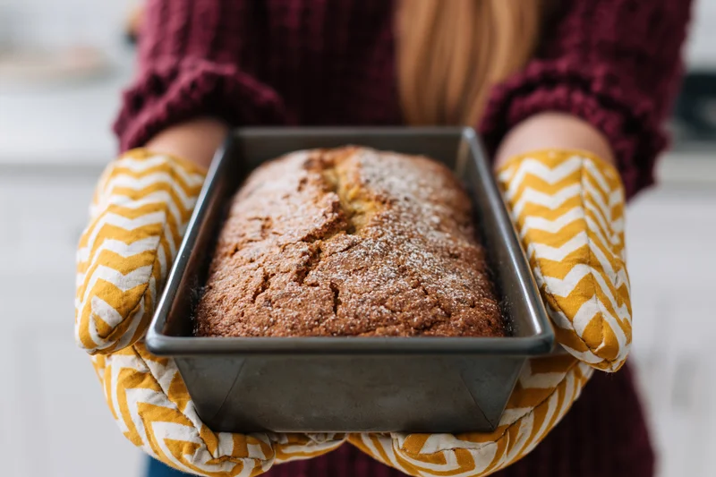 Woman holding freshly baked loaf in oven mitts in kitchen