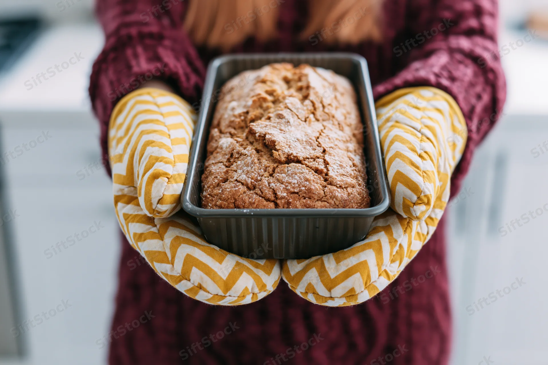 Woman holding freshly baked bread in oven mitts in kitchen