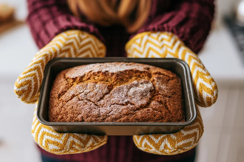 Woman holding freshly baked bread in oven mitts in kitchen