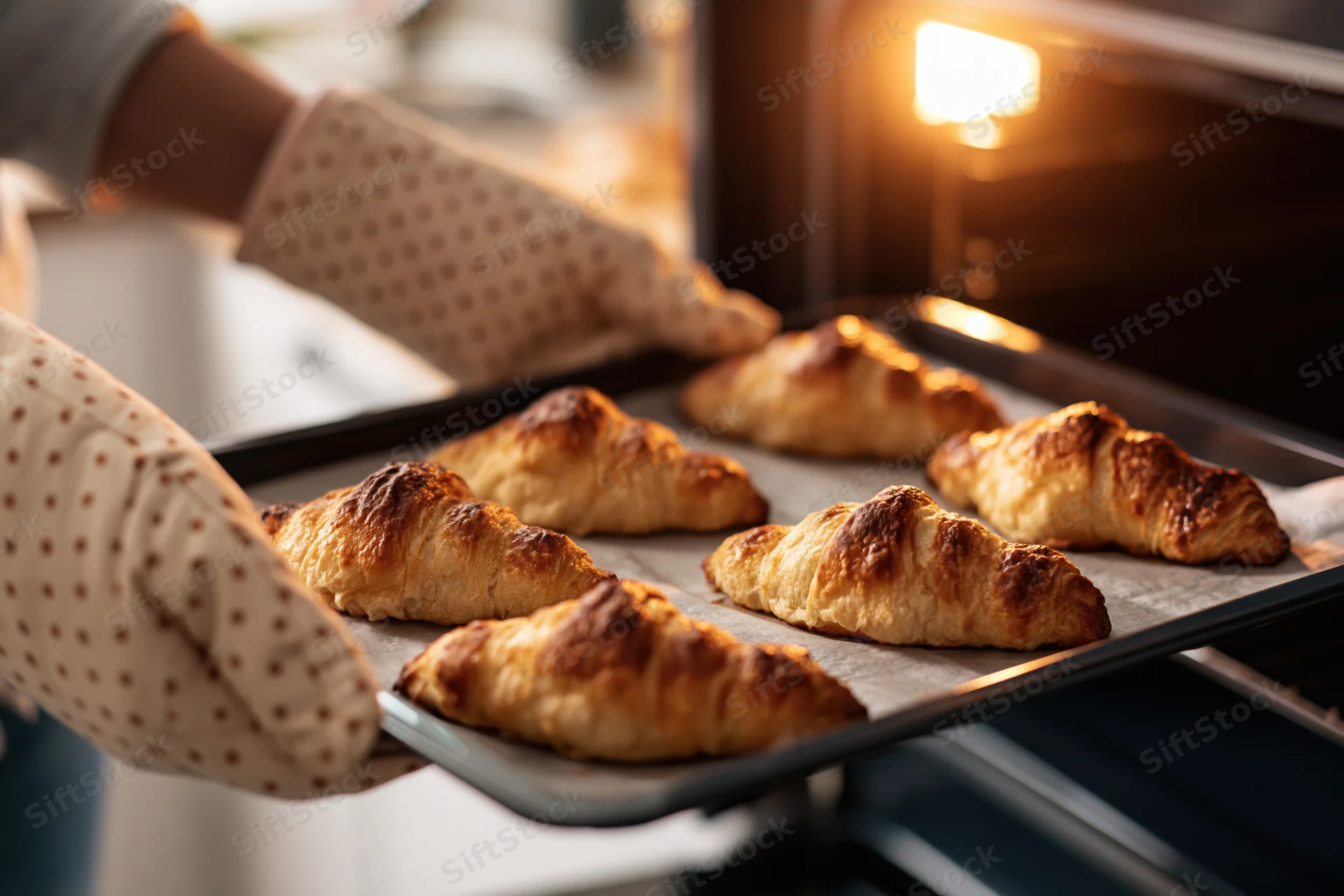 Woman removing tray of golden baked croissants from oven in kitchen