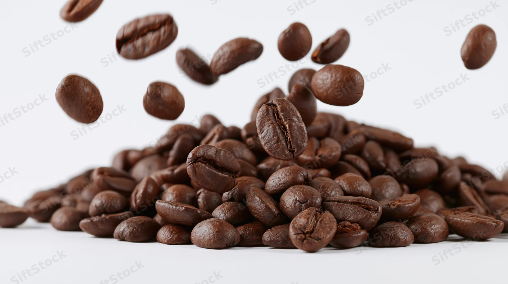 Roasted coffee beans falling into a pile on a white background