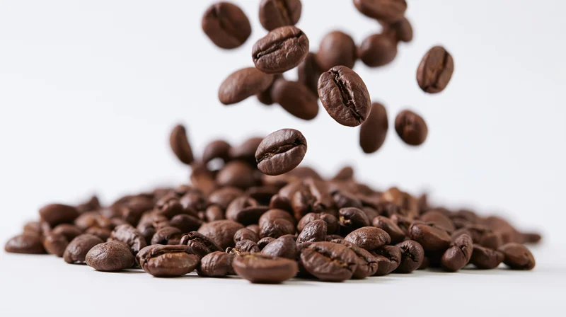Roasted coffee beans falling onto a pile on a white surface