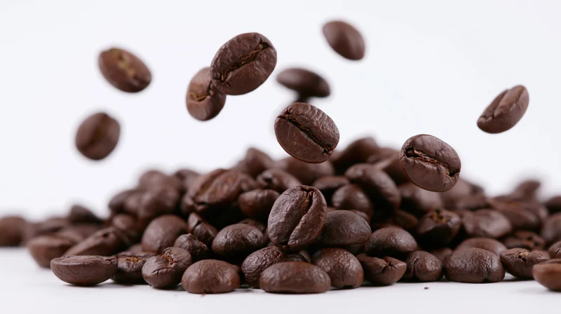 Roasted coffee beans falling onto a pile against a white background