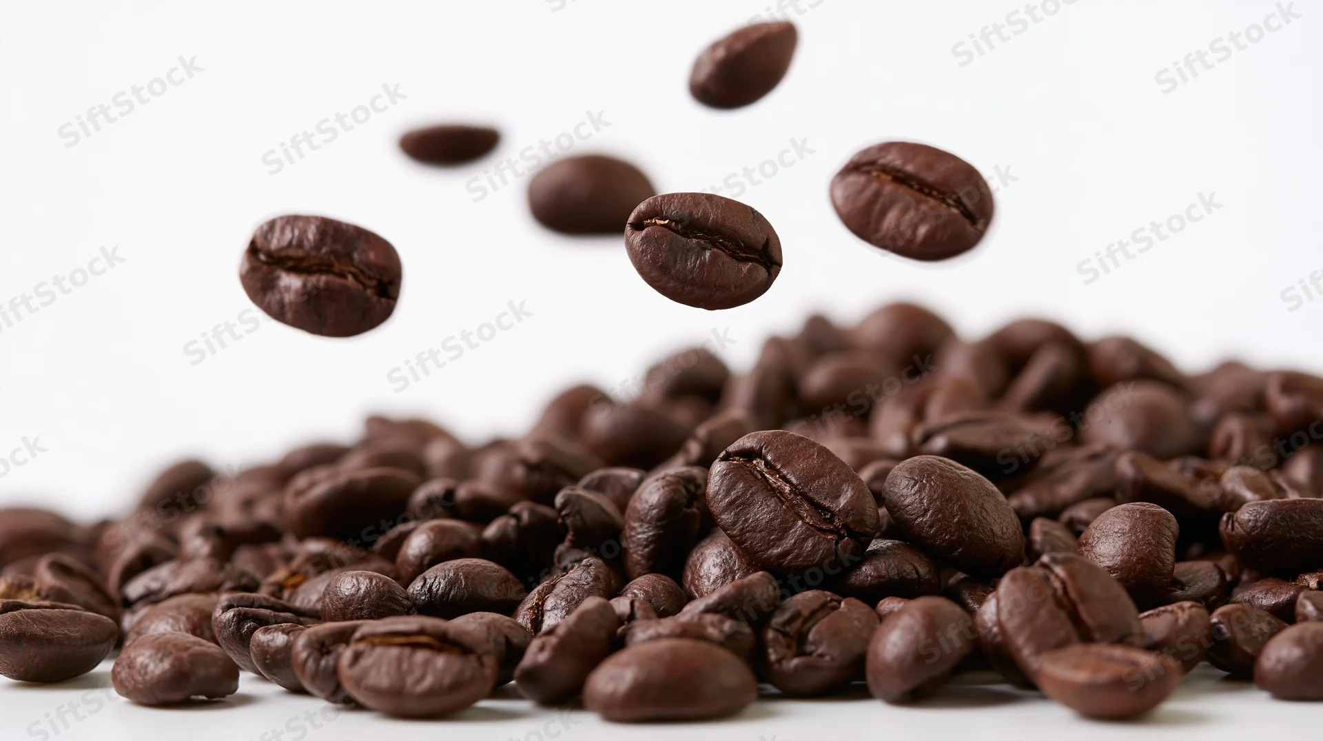 Roasted coffee beans falling onto a pile against a white background
