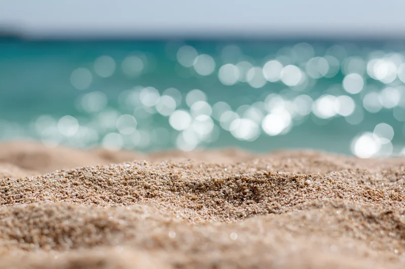 Closeup of textured sand on a beach with sparkling ocean in the background