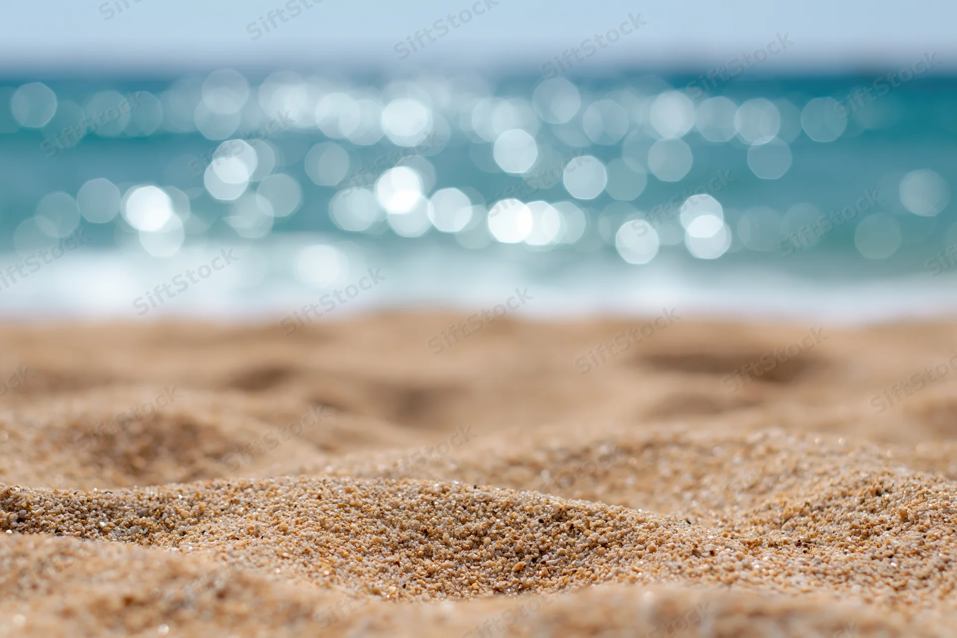 Closeup of textured sand on a beach with sparkling ocean in the background