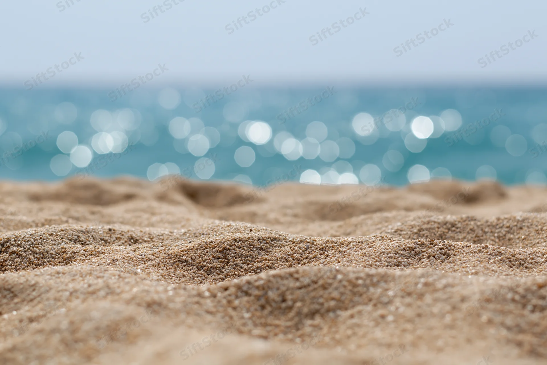 Close-up of textured sand on a beach with sparkling ocean in the background