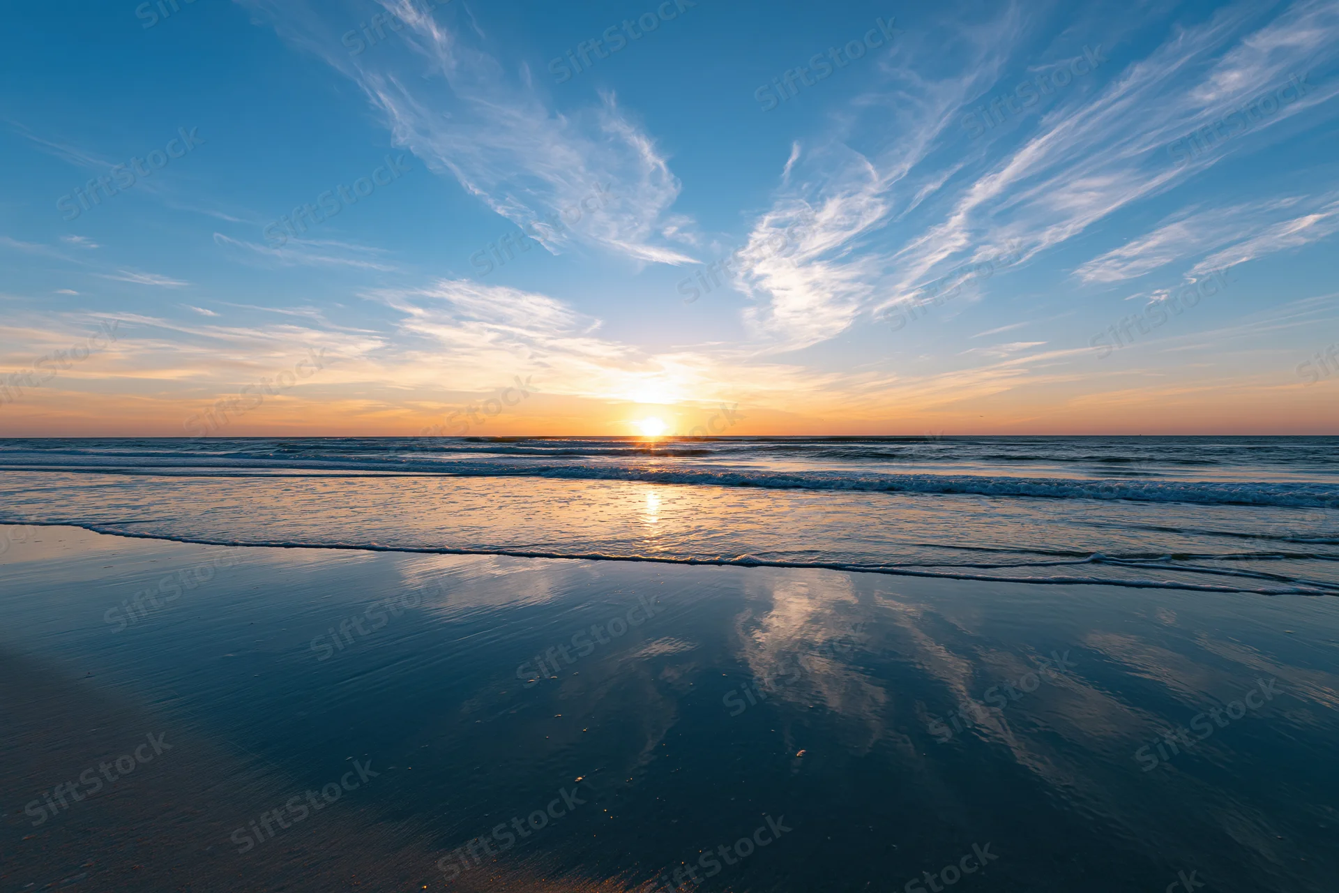 Sunset over ocean reflecting on wet sand at beach horizon
