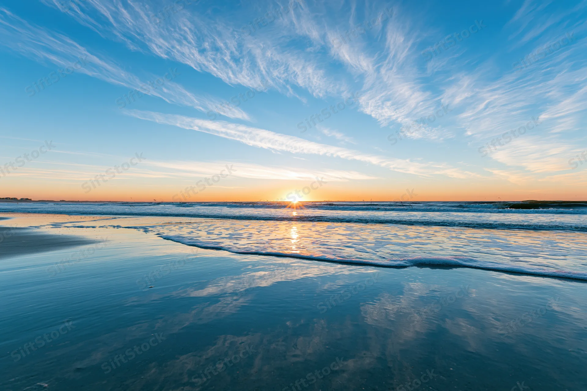 Sunset over the ocean reflecting on wet sand at the beach