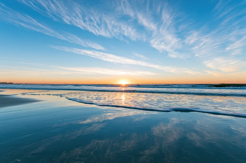 Sunset over the ocean reflecting on wet sand at the beach