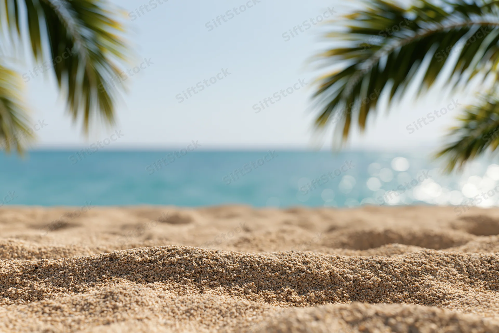 Close-up of textured sand on a tropical beach with palm fronds framing the ocean view