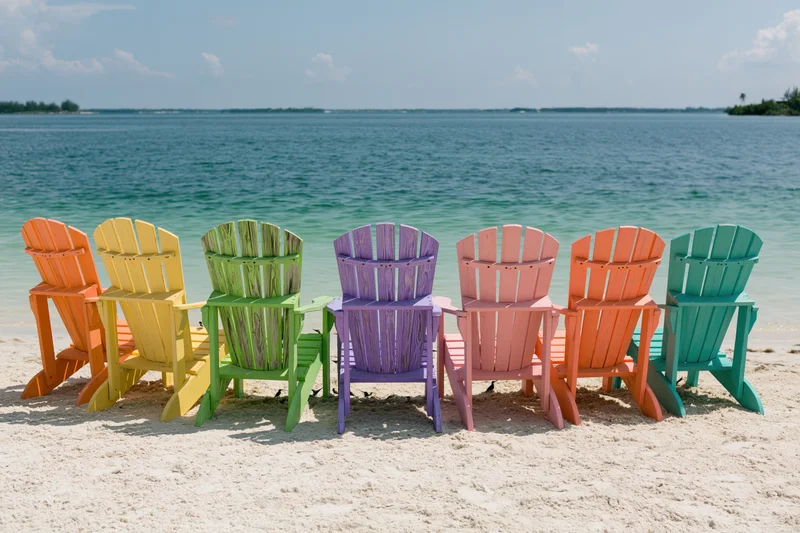Row of colorful adirondack chairs on sandy beach facing ocean