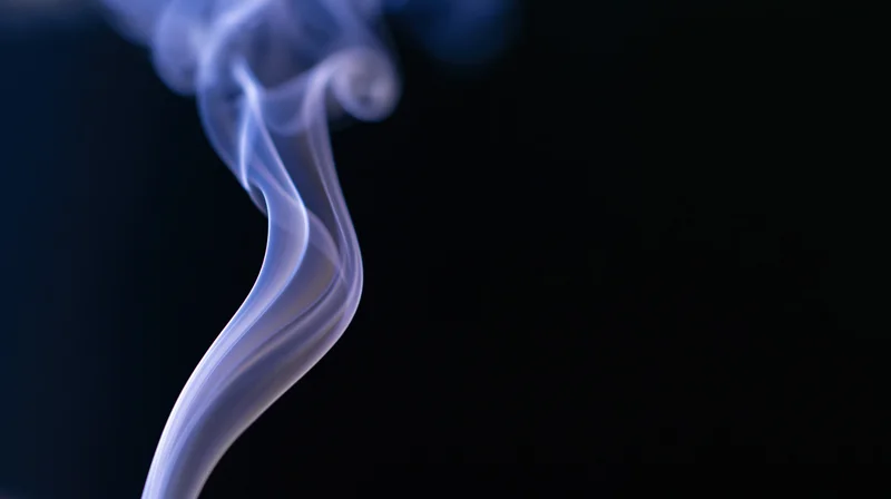 Curling blue smoke rising against a dark background with copyspace on the right