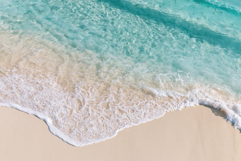 Waves breaking on a sandy beach with turquoise water viewed from above
