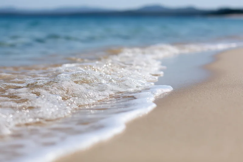 Gentle wave washing over sandy beach at shoreline