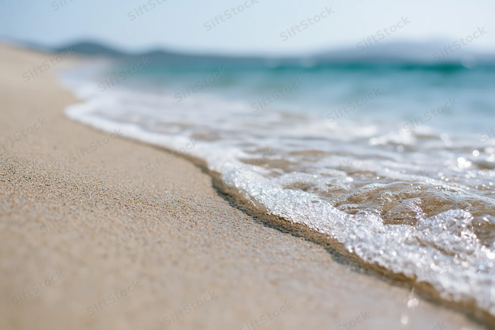 Gentle wave washing over sandy beach at shoreline