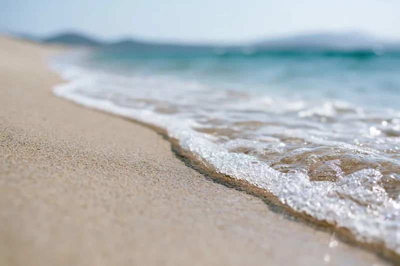 Gentle wave washing over sandy beach at shoreline