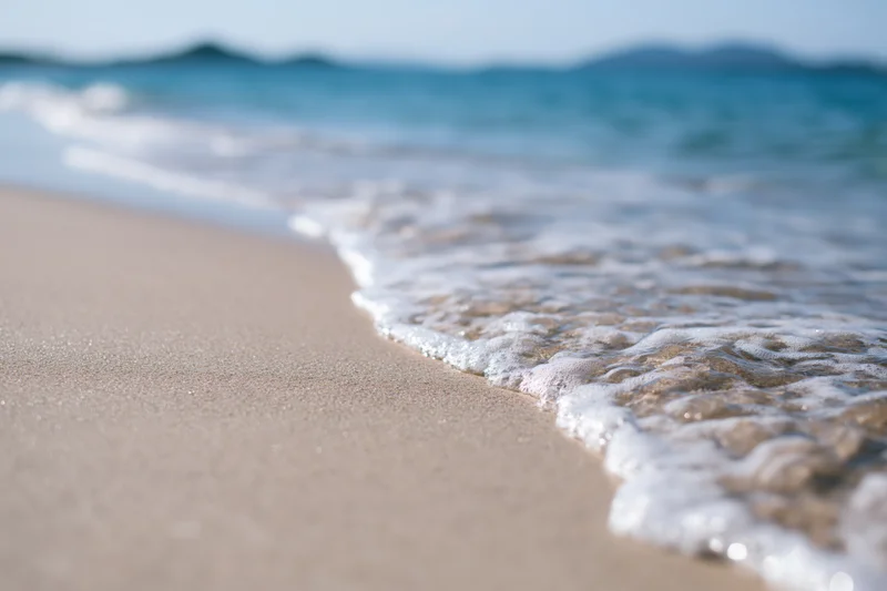 Gentle wave with white foam washing over sandy beach at shoreline