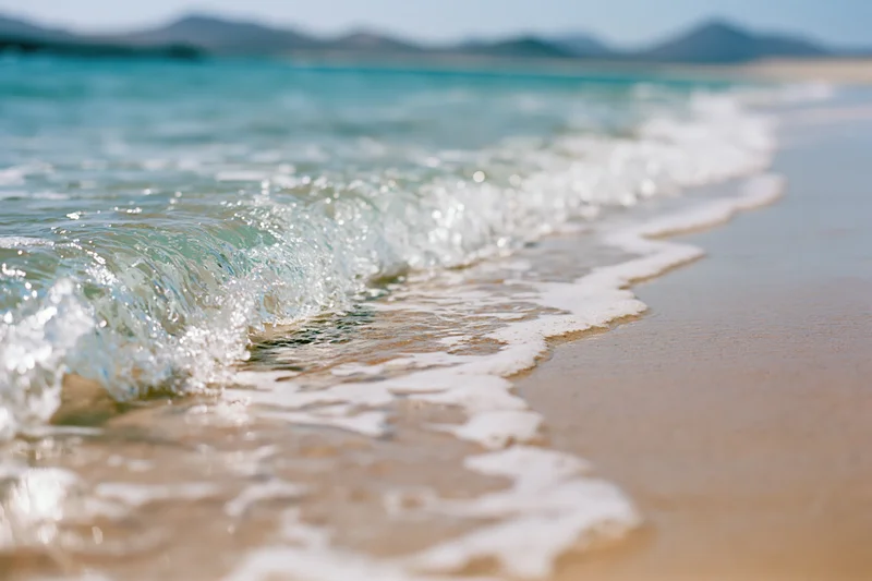Gentle wave breaking on sandy beach with turquoise water and distant mountains in background