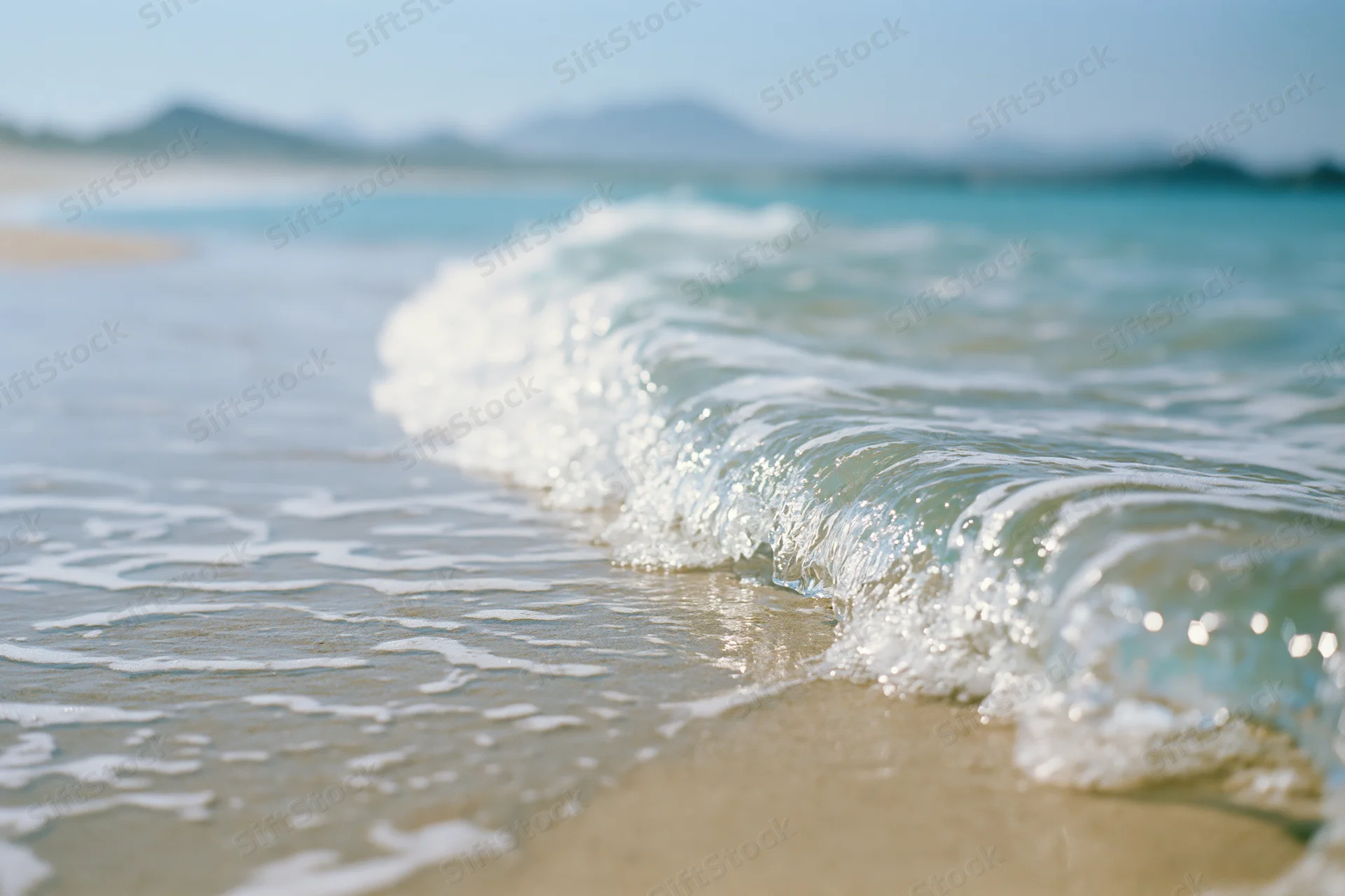 Gentle wave breaking on sandy beach with distant mountains under clear sky