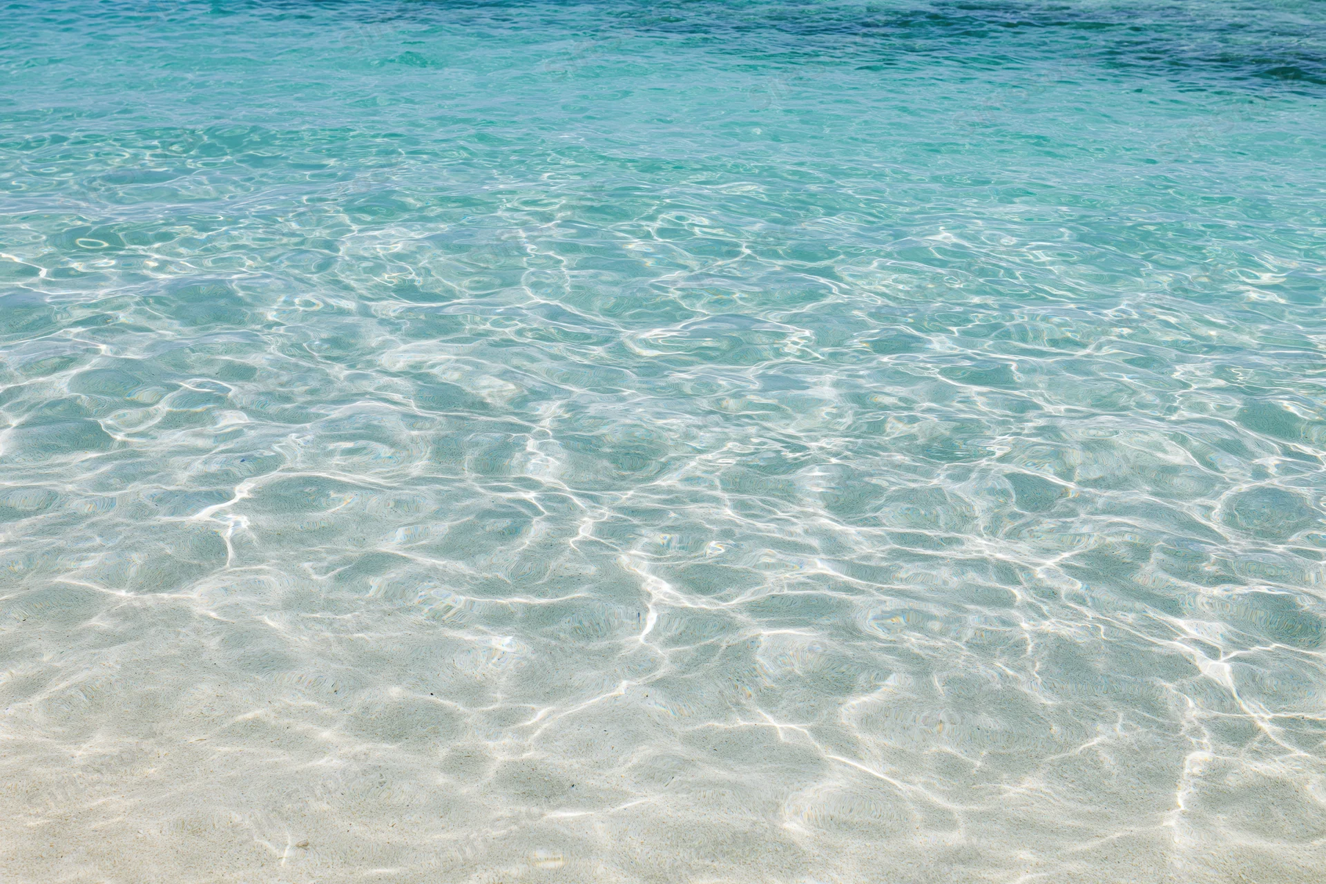 Clear turquoise ocean water rippling over white sand at shallow beach